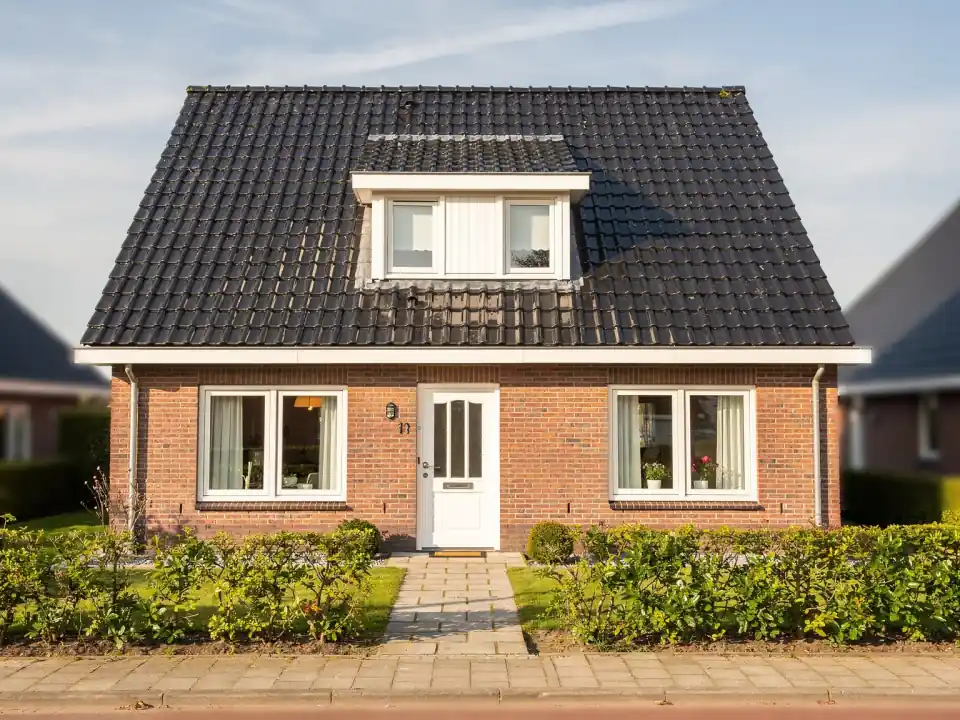 Dezelfde woning na de dak- en gevelreiniging: donkere schone pannen, frisse bakstenen en wit houtwerk